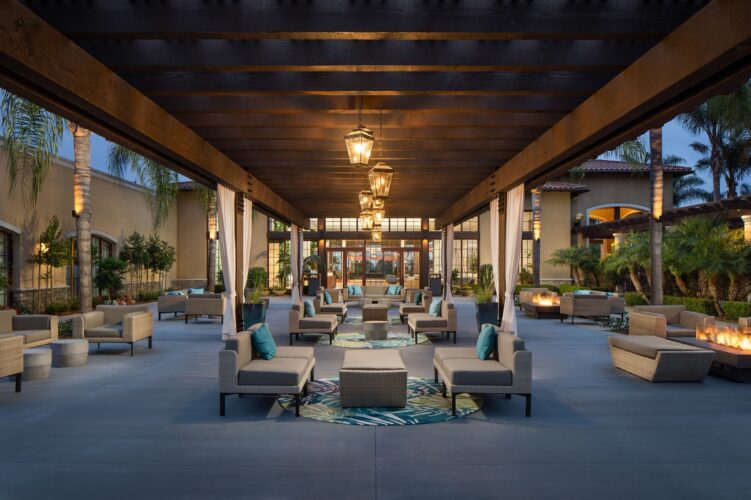 The image shows the Palm Courtyard at The Westin Carlsbad Resort & Spa, featuring an expansive outdoor lounge area under a wooden pergola 